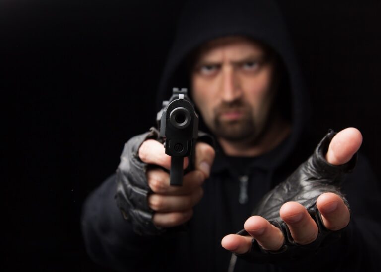 Robber,With,Gun,Holding,Out,Hand,Against,A,Black,Background