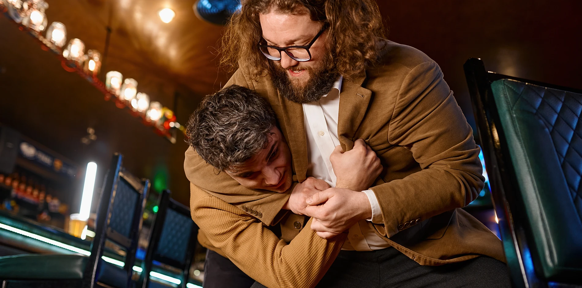 A bearded man, Assault, grips a younger man's neck and arm in a dim bar.