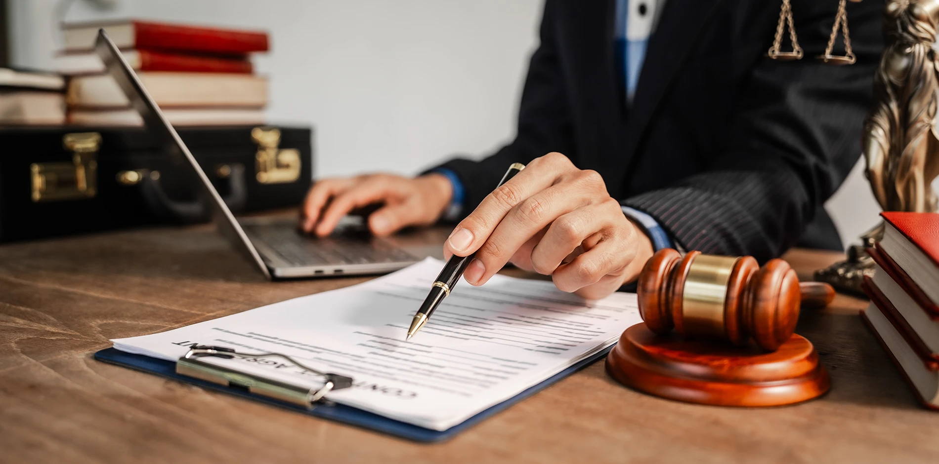 A civil law professional points a pen at a document on a desk with a laptop, gavel, books, and Lady Justice statue.