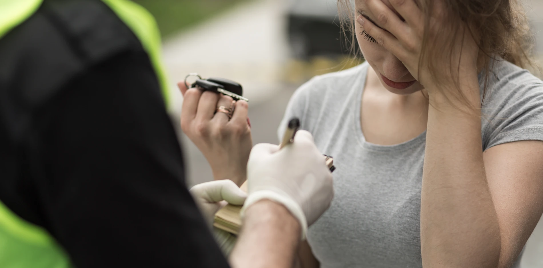 Distressed woman with car keys covers her face as a gloved officer writes on a pad.