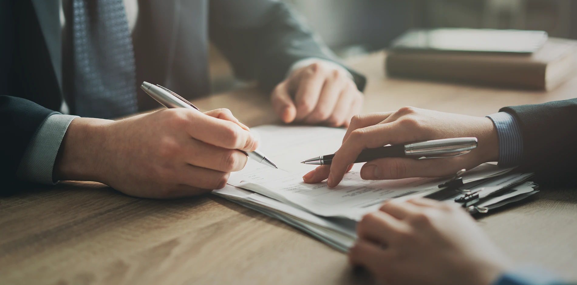 Two hands write and point at documents on a desktop during modifications.