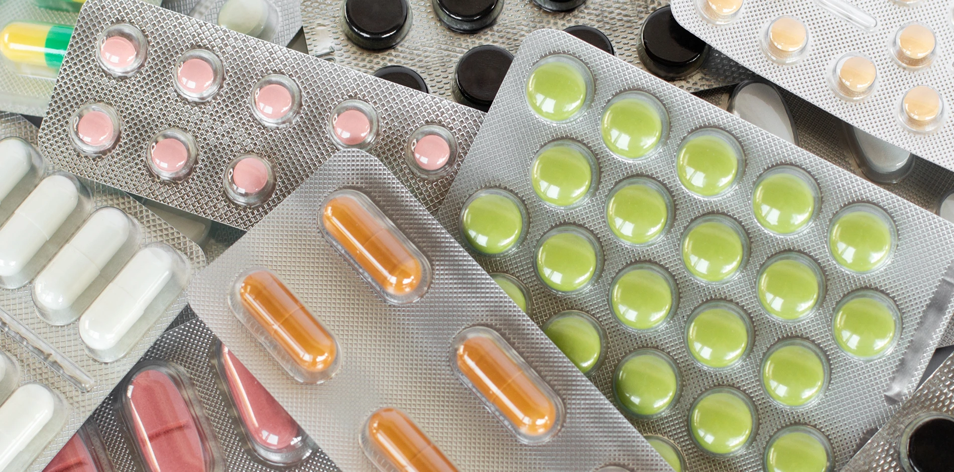 Assorted prescription drug blister packs with green, pink, orange, white, and black pills and capsules.