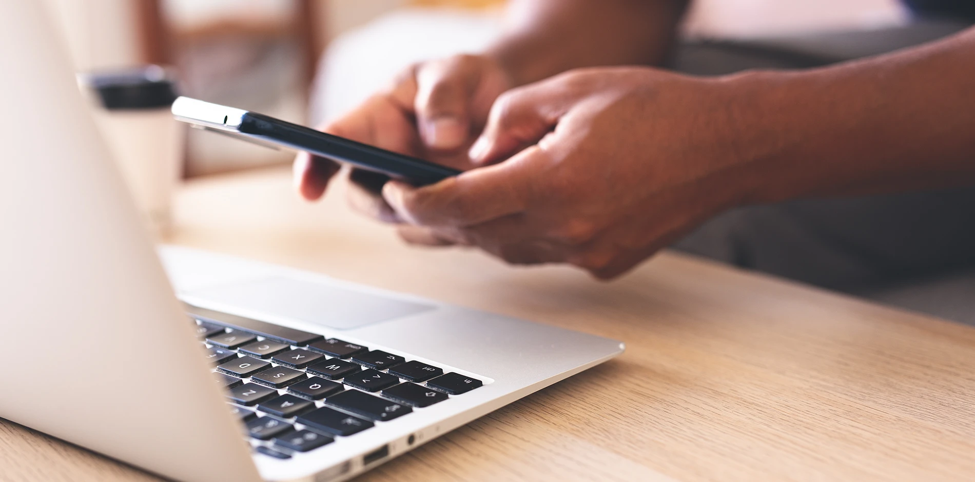 Student uses a smartphone and laptop on a light wood desk.