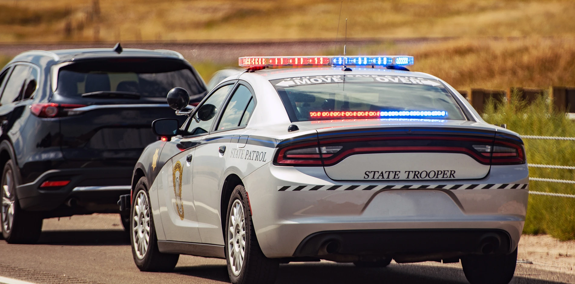White State Patrol car with red and blue lights flashing, stopped behind a black SUV on a road.