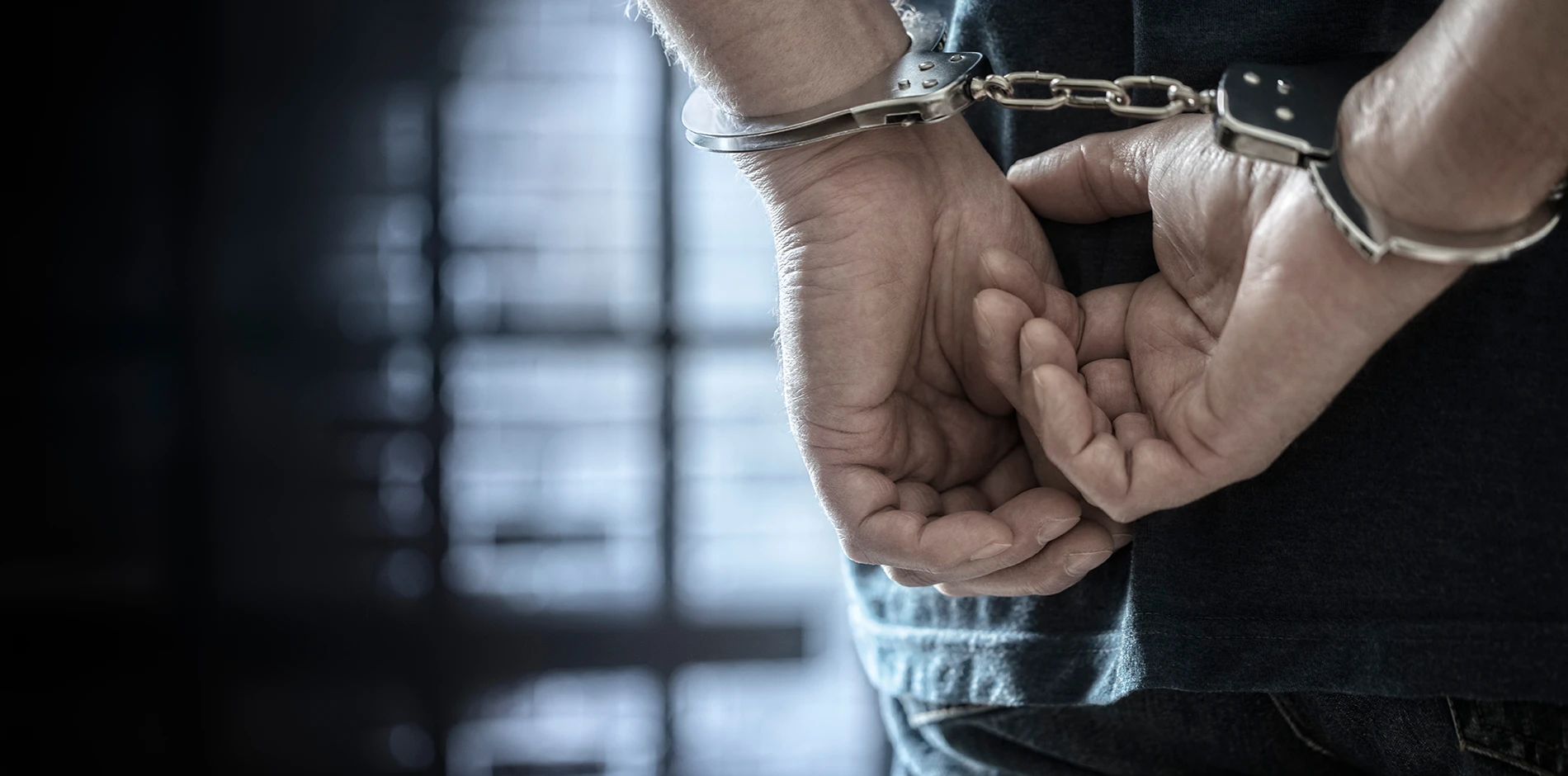Violent Desktop stands with hands handcuffed behind their back against a dark, blurred background.